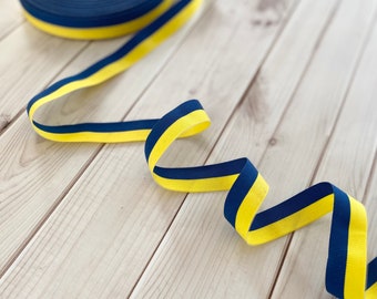 May include: A blue and yellow striped ribbon with a slight curl. The ribbon is on a light wood surface.
