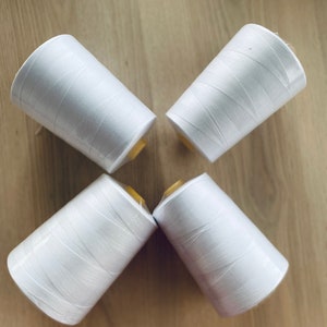 May include: Four spools of white thread are arranged in a cross pattern on a wooden surface.