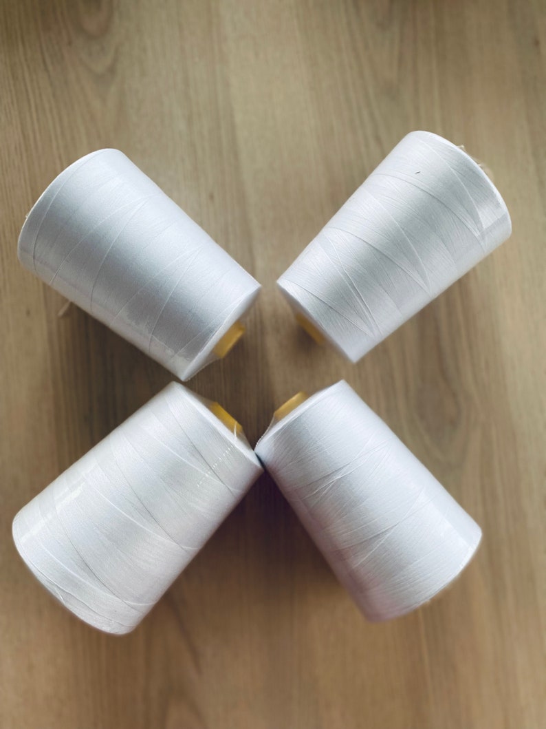 May include: Four spools of white thread are arranged in a cross pattern on a wooden surface.