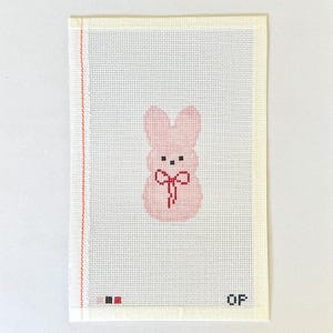 May include: A needlepoint canvas featuring a pink bunny with a red bow. The bunny has black eyes and is centered on a white background. The canvas has a red stitched border on the left side and the letters "QF" in the bottom right corner.