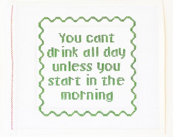 May include: White canvas with a green embroidered quote that reads "You can't drink all day unless you start in the morning". The quote is surrounded by a green scalloped border.