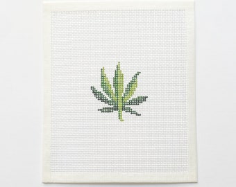 May include: A white canvas with a green marijuana leaf embroidered on it.