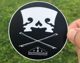 May include: Black and white sticker featuring a skull made from a violin's f-hole and two crossed violin bows. The text "La Hacienda Musica" is at the bottom of the sticker.
