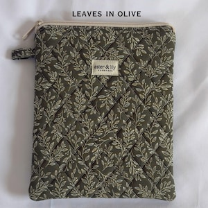 May include: A rectangular olive green zipped pouch featuring a quilted diamond pattern and a white leaf print. A small fabric tag labelled aster & lily is centred on the front. The text LEAVES IN OLIVE is printed above the pouch.
