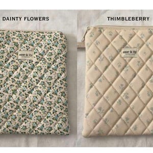 May include: Two rectangular quilted pouches with zips. The left pouch, labelled DAINTY FLOWERS, has a dense blue and green floral print. The right pouch, labelled THIMBLEBERRY, has a sparse floral print. Both feature an aster & lily label.