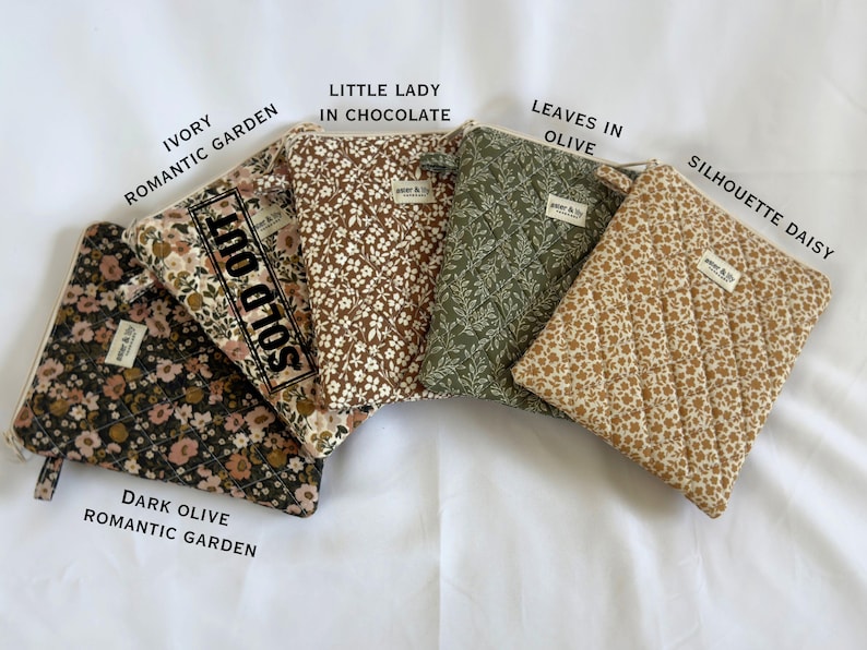May include: Four quilted pouches with zip closures and small fabric labels reading 'pear & lily'. Patterns include dark olive floral, ivory floral marked 'SOLD OUT', chocolate brown floral, olive green leaves, and tan daisy print.