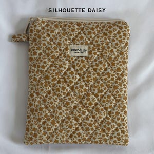 May include: A rectangular quilted pouch featuring a mustard yellow and white floral pattern. The top includes a zip closure and a small fabric tab. A rectangular label in the centre reads aster & lily HANDMADE. Text above reads SILHOUETTE DAISY.