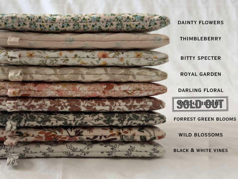May include: A stack of nine quilted fabric pouches with various floral and vine patterns. Text labels include Dainty Flowers, Thimbleberry, Bitty Specter, Royal Garden, Darling Floral, Sold Out, Forrest Green Blooms, Wild Blossoms, and Black & White Vines.