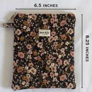 May include: A quilted pouch with a dark floral pattern in shades of pink, brown, and cream. It features a zip closure, a small side tab, and a label reading aster & lily. Dimensions are 16.51 cm wide by 20.96 cm high.