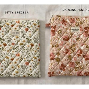 May include: Two rectangular quilted pouches with zips. The left pouch, labelled BITTY SPECTER, features a white fabric with a scattered orange and green floral print. The right pouch, labelled DARLING FLORAL, has a dense pink and brown floral pattern. Both have an aster & lily label.