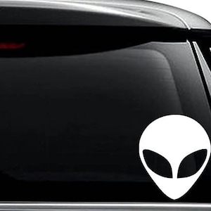 May include: White alien head silhouette sticker for a car window. The sticker is on a black car window.