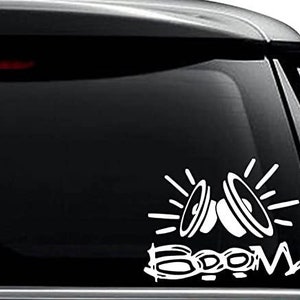 May include: White vinyl decal featuring two stylized speakers with radiating lines and the word "BOOM" in a bold font. The decal is designed to be applied to a car window or similar surface.