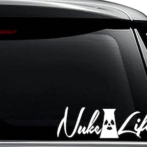 May include: White vinyl decal sticker with the text "Nuke Life" in a cursive font. A stylized image of a nuclear power plant is between the words.
