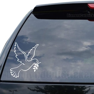 May include: White vinyl decal of a dove carrying an olive branch, a symbol of peace. The decal is applied to the rear window of a black car.