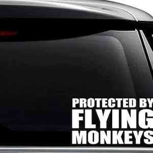 May include: White vinyl decal with the text "Protected by Flying Monkeys" on a black car window.