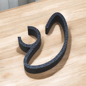 Puede incluir: Un soporte para teléfono de plástico negro con forma de letra 'S' estilizada.