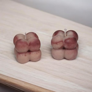 May include: Two brown and beige bubble candles with a single wick on a wooden surface.