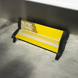 Könnte beinhalten: Eine gelbe Bank mit schwarzen Metallbeinen. Die Bank hat einen weißen Streifen und eine Werbung für "ACE ROLLING" auf der Rückseite.
