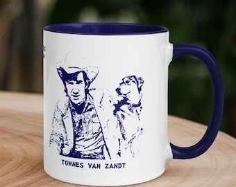 May include: White ceramic coffee mug with a blue rim and handle. The mug features a blue silhouette of singer-songwriter Townes Van Zandt with his dog. The text "Townes Van Zandt" is printed in blue at the bottom of the mug.