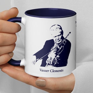 May include: White ceramic coffee mug with a navy blue rim and handle. The mug features a silhouette of a person playing the violin with the text "Vasser Clements" at the bottom.