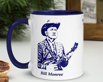 May include: White ceramic mug with a blue rim and handle. The mug features a blue silhouette of Bill Monroe playing a mandolin. The text "Bill Monroe" is printed in blue at the bottom of the mug.