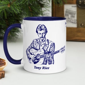 May include: White ceramic coffee mug with a blue rim and handle. The mug features a blue and white illustration of a man playing a guitar with the text "Tony Rice" below the image.