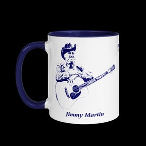 May include: White ceramic coffee mug with a blue rim. The mug features a blue silhouette of a country music singer playing a guitar. The text "Jimmy Martin" is printed in blue at the bottom of the mug.
