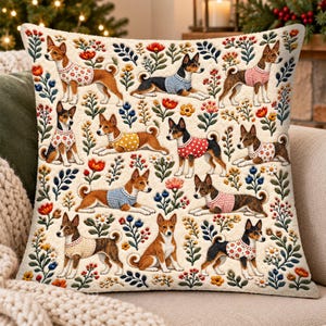 May include: A square throw pillow featuring a cream-colored background with a repeating pattern of Basenji dogs wearing various sweaters, interspersed with colorful floral motifs including red, orange, and blue flowers and green foliage.