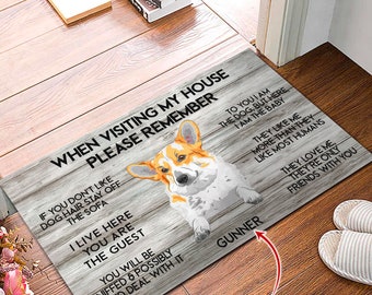 May include: A wooden doormat with a white and brown woodgrain pattern. The doormat features a cartoon image of a corgi dog with the text "When visiting my house please remember" and "Gunner" in black text. The doormat also includes the text "If you don't like dog hair stay off the sofa I live here you are the guest you will be sniffed & possibly licked deal with it To you I am the dog but here I am the baby They like me more than they like most humans They love me they're only friends with you Custom name".