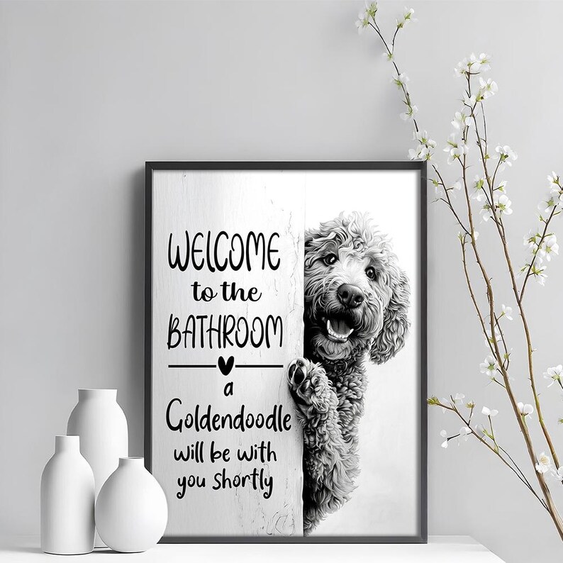 以下が含まれることがあります： 「WELCOME to the BATHROOM」の文字とゴールデンレトリバーが描かれた黒いフレームの壁掛けアート。 「a Goldendoodle will be with you shortly」の文字も含まれています。 白い花瓶と花の枝が前景にあります。