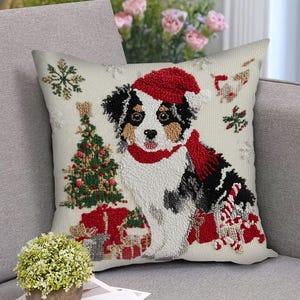May include: A square cushion with a festive Christmas design. The cushion depicts a dog wearing a Santa hat and scarf, alongside a Christmas tree and presents. The colour scheme includes red, green, black, white, and beige.