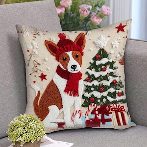 May include: A decorative Christmas throw pillow featuring a dog wearing a red hat and scarf. The dog sits next to a decorated Christmas tree and wrapped gifts. The pillow has a beige background with embroidered details and red star accents.
