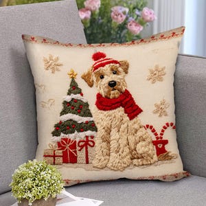 Op de afbeelding: Vierkant decoratief kussen met een kerstthema. Het kussen heeft een geborduurd beeld van een hond met een rode sjaal en muts, zittend naast een kerstboom en cadeaus. Sneeuwvlokken en zuurstokken zijn ook op het kussen geborduurd.
