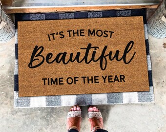 May include: A brown doormat with the text "It's the most beautiful time of the year" in black lettering.