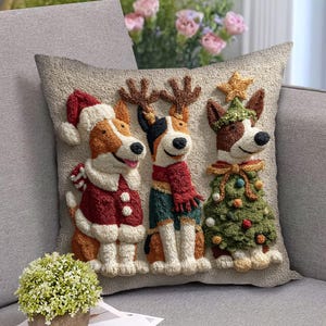 May include: A decorative square pillow featuring three dogs dressed in Christmas attire. One dog wears a Santa hat and coat, another has reindeer antlers and a scarf, and the third is a Christmas tree. The pillow is beige with a textured design.