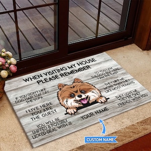 May include: A welcome mat with a brown and white dog peeking over the top. The mat has a woodgrain background and the text "When visiting my house please remember" and "To you I am the dog, but here I am the baby" and "They like me more than they like most humans" and "They love me, they're only friends with you".