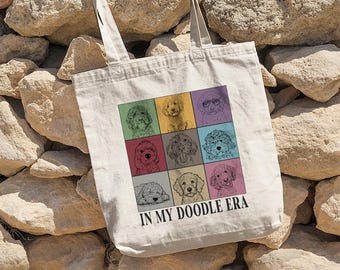 May include: A white canvas tote bag featuring a colourful design of doodle dogs. The text "IN MY DOODLE ERA" is printed on the bag.