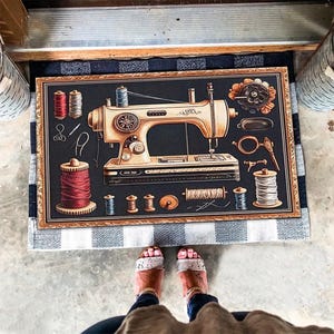 Pode incluir: Um tapete de porta de estilo vintage com uma máquina de costura em fundo preto e moldura dourada. O tapete apresenta uma máquina de costura, carretéis de linha, agulhas e outras ferramentas de costura.