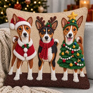 May include: A square throw pillow featuring a textured punch needle design of three dogs. The left dog wears a Santa hat and cape. The center dog wears reindeer antlers and a red scarf. The right dog wears a Christmas tree costume with a star.