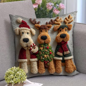 Pode incluir: Uma almofada decorativa cinzenta com três personagens de Natal de pelúcia. Um cão com chapéu e casaco de Pai Natal segura uma bengala de doces. Duas renas usam uma árvore de Natal e um cachecol. A almofada está num sofá cinzento.