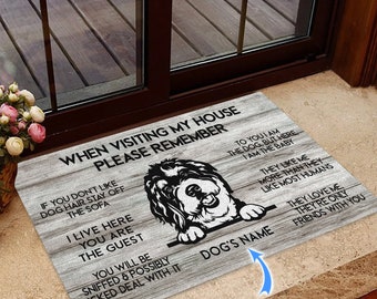 May include: A brown and white wooden doormat with a black and white dog illustration. The doormat has the text "When visiting my house please remember" and "To you I am the dog, but here I am the baby". The doormat also has the text "Dog's Name" and "Custom Name".