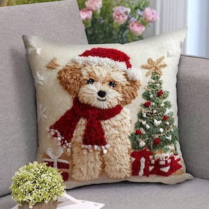 May include: Embroidered Christmas pillow featuring a light brown and white puppy wearing a red Santa hat and scarf. A green Christmas tree with red ornaments and a gold star is next to the puppy. Presents are at the bottom.