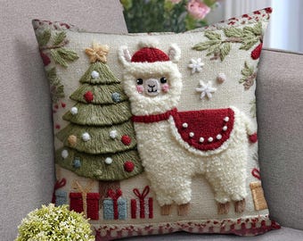 Op de afbeelding: Geborduurd kerstkussen met een witte lama met een rode hoed en zadel, naast een groene kerstboom. Het kussen heeft een crèmekleurige achtergrond met sneeuwvlokken, cadeaus en een ster.