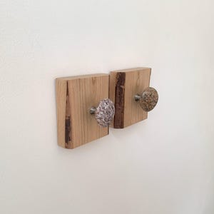 May include: Two wooden wall hooks with stone knobs. The hooks are made of reclaimed wood and have a natural finish. The knobs are a light brown and a light gray with brown speckles.