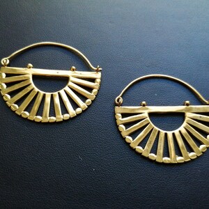 May include: A pair of gold hoop earrings with a sunburst design. The earrings are made of metal and have a circular shape with a semi-circular cutout in the center.