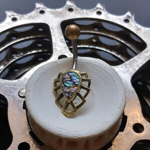 May include: A gold belly button ring with a teardrop-shaped iridescent abalone shell set in a geometric design.