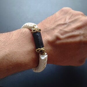 May include: A white bone bracelet with a black and brown accent. The bracelet is made of carved bone and has a natural, organic look.