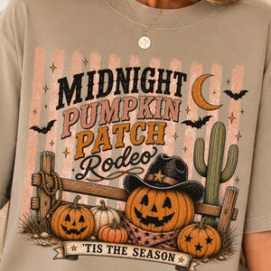 May include: A beige t-shirt featuring a graphic with the text "MIDNIGHT PUMPKIN PATCH RODEO" and "'TIS THE SEASON". The design includes a jack-o'-lantern wearing a cowboy hat, a cactus, a crescent moon, bats, and a wooden fence background.