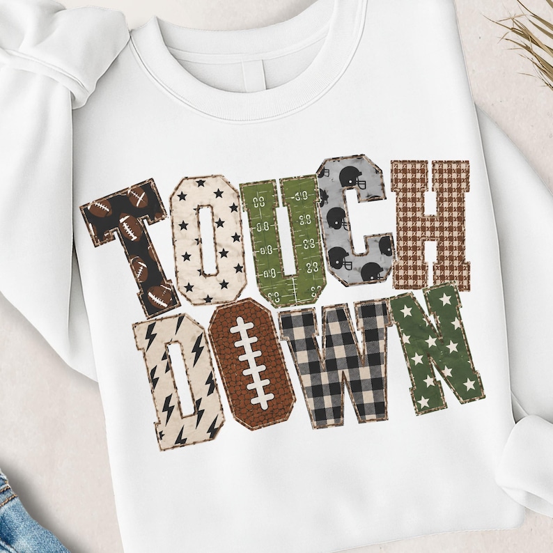 May include: A white crewneck sweatshirt featuring the word TOUCHDOWN in large block letters. Each letter has a unique pattern including footballs, stars, field markings, helmets, plaid, lightning bolts, and a textured brown football shape.