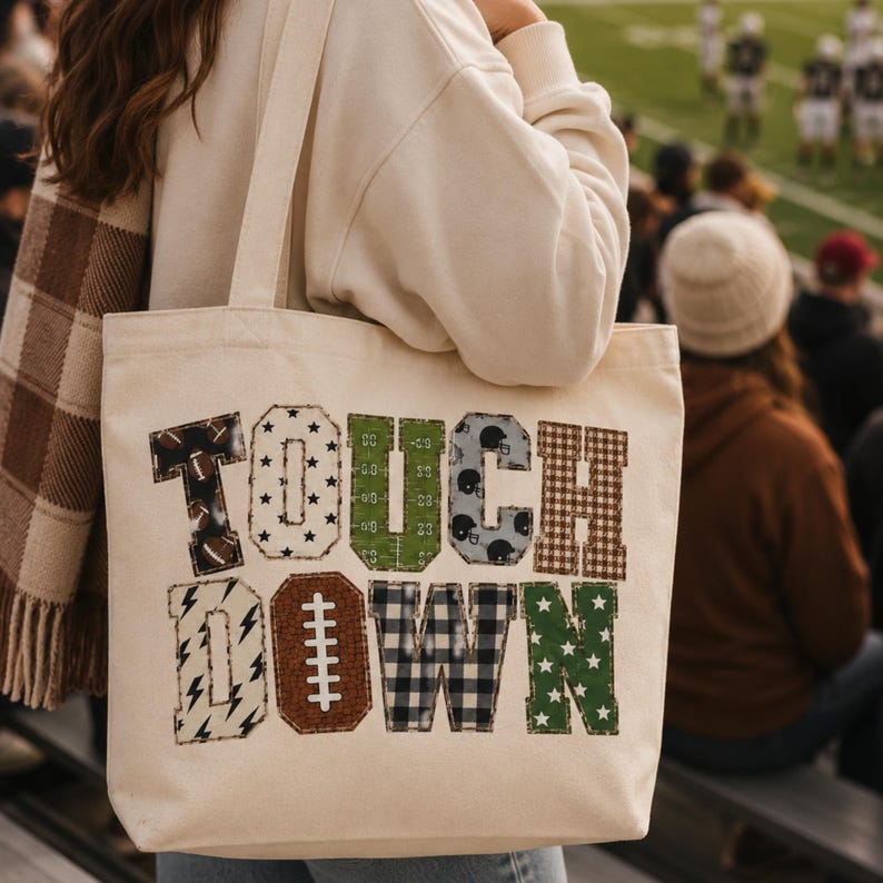 May include: A cream-colored canvas tote bag featuring the word TOUCHDOWN in large, block-style letters. Each letter displays a unique pattern, including footballs, stars, a field grid, helmets, plaid, lightning bolts, and buffalo check.